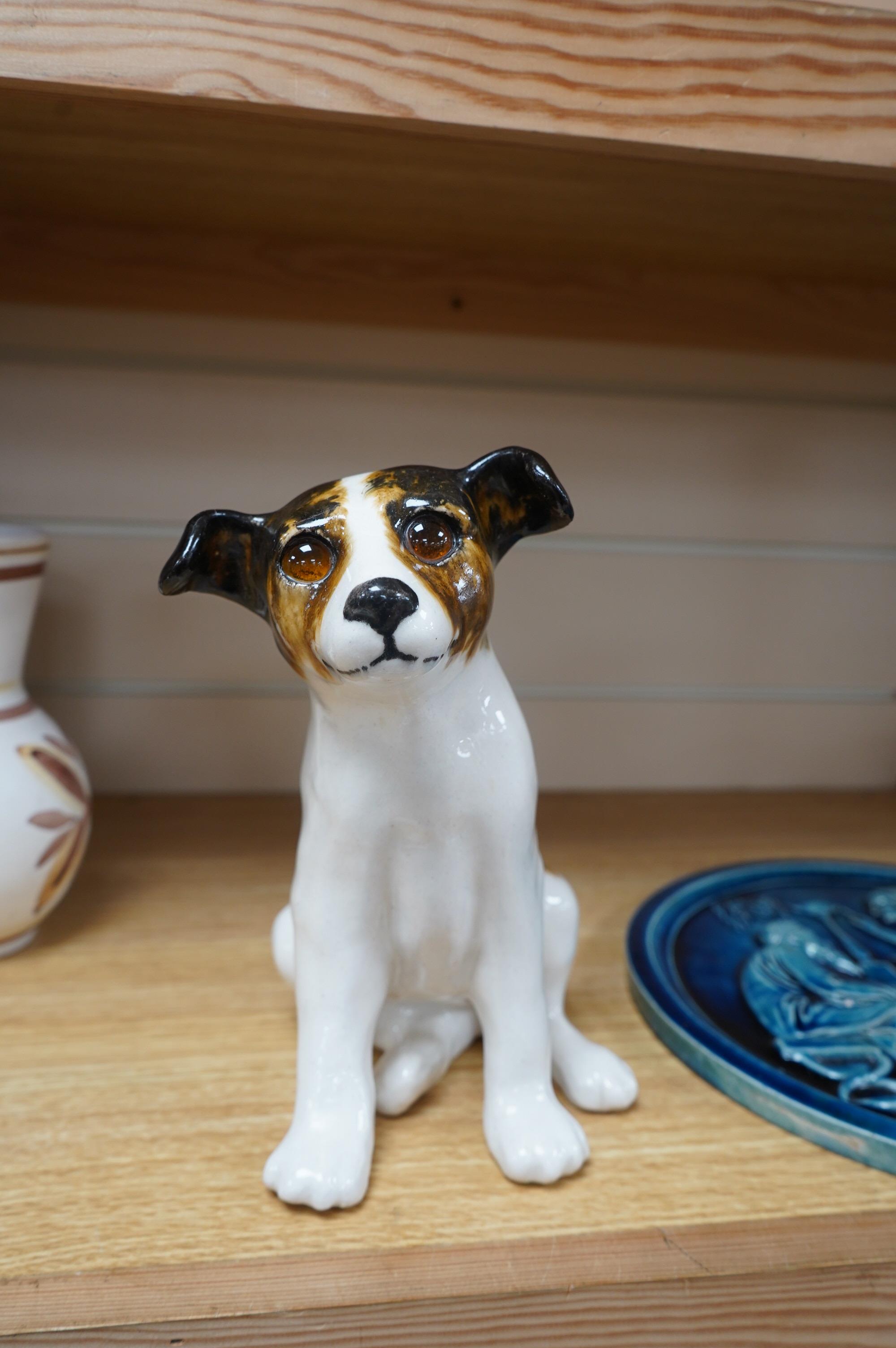 A Copenhagen P Ipson circular glazed plaque, representing Winter/Ages of Man, and a J. Winstanley pottery seated dog with glass eyes, largest 27cm in diameter. Condition - good, the right ear of the Winstanley dog has be